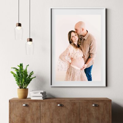 framed photo of pregnant couple cuddling on blue wall over couch