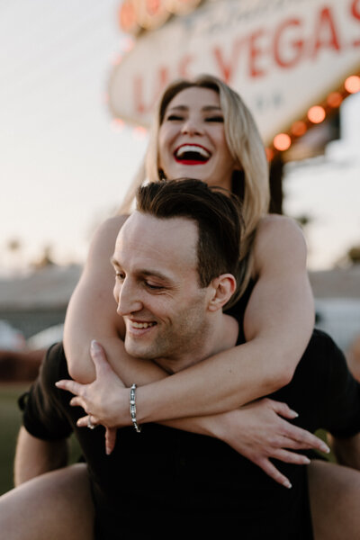 A person on their partner's back as they both smile 