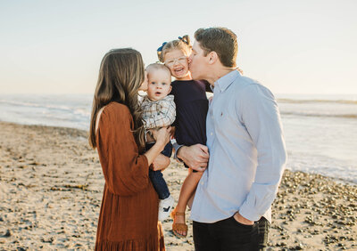 Image depicting a mom kissing son while dad is holding him during family photos