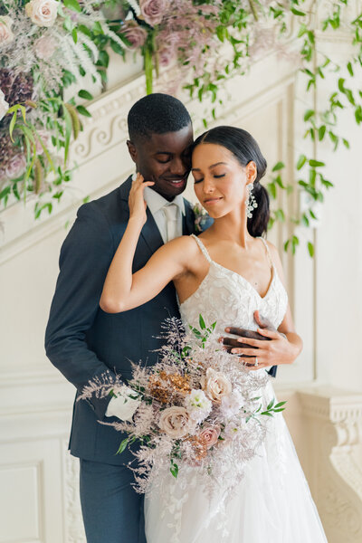 Wedding photograph taken in front of  the doors of historic downtown staunton virginia venue with period architecture decorated in vines and florals. The couple is embracing and smiling at one another.