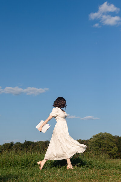 a woman runs in a grass field holding her laptop in hand