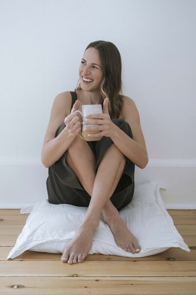 Woman practicing mindfulness, sitting on a cushion with a cup of tea, laughing joyfully.