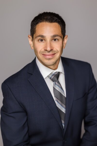 Professional corporate headshot of a business man in a navy suit and striped tie on a gray background:  Long Island team headshots.