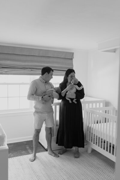 Black and white image of  parents with their twins next to cribs