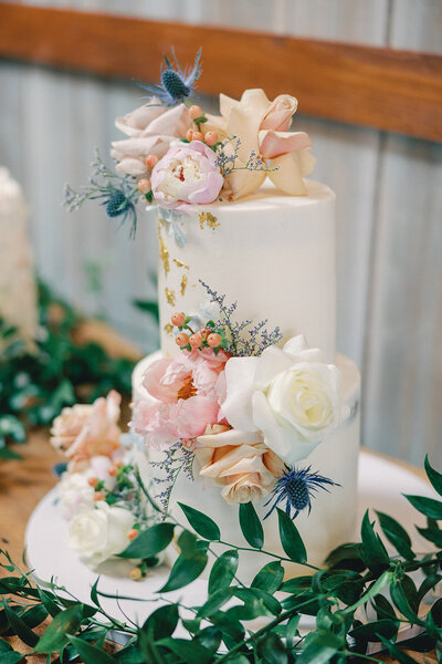 White tiered wedding cake decorated with  pink flowers and greenery