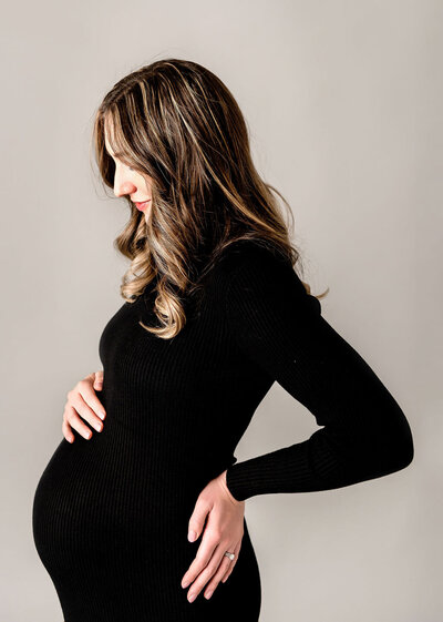 Professional maternity photography by Stamford CT photographer showcasing pregnant woman in elegant black ribbed dress during studio session