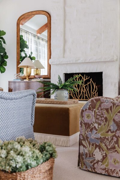An angular view of a styled living room with floral patterned chairs and lots of plants.
