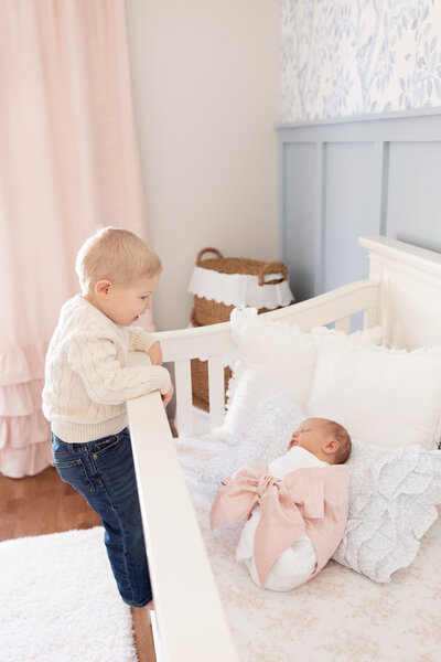 Big brother watching new baby sister in the crib