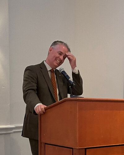 Adrian standing at a lectern speaking at an event