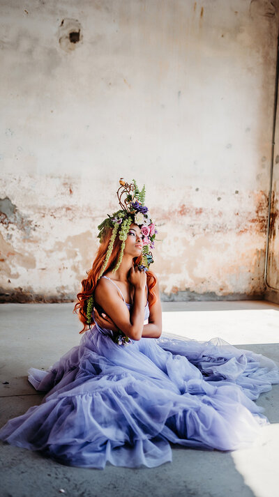 a photo of a model sitting on the floor in a purple dress with a beautiful headpiece