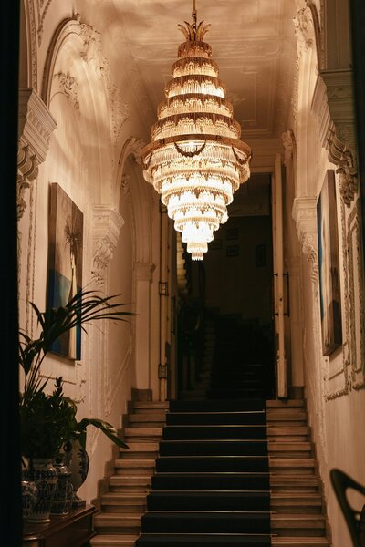 Ornate hallway staircase with a grand chandelier overhead