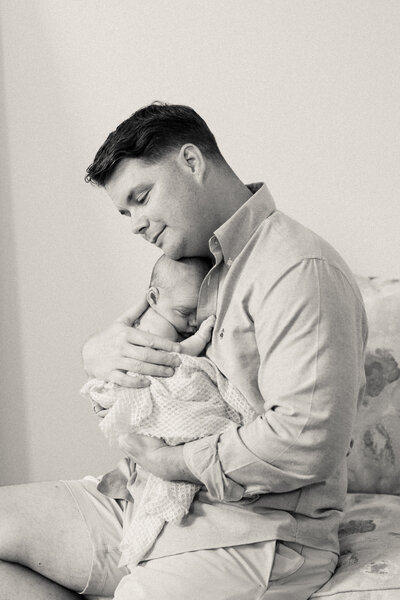 Dad holds his newborn son close to his chest and closes his eyes