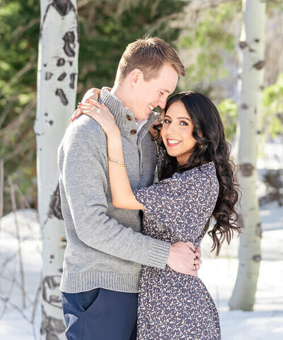 engaged couple standing in the snow holding each other