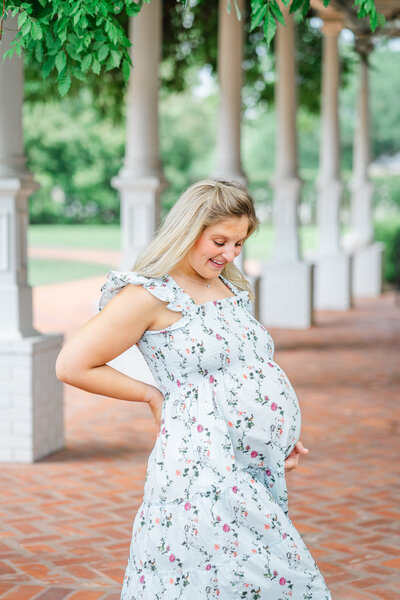 A pregnant mother stands by a row of columns in the courtyard of Woodbine Mansion in Round Rock, TX, captured by a Round Rock Maternity Photographer.