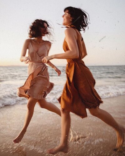 Two women running on beach in dresses