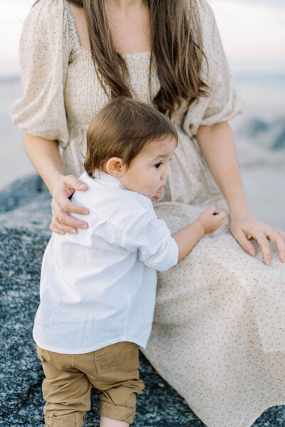 mother in a christy dawn dress with her son sitting on rocks on the beach by Richmond va Family Photographer