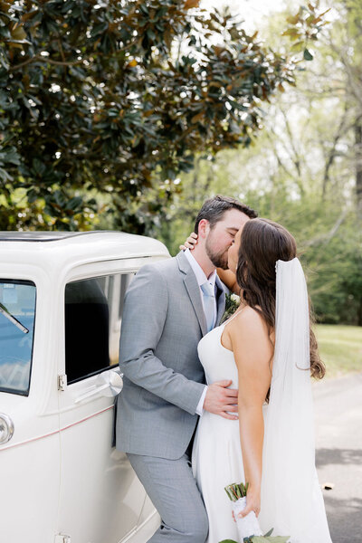 couple kissing on their wedding day next to a vintage car 