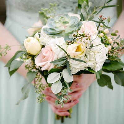 Close up of a bridesmaid in a sea green dress holding beachy floral bouquet