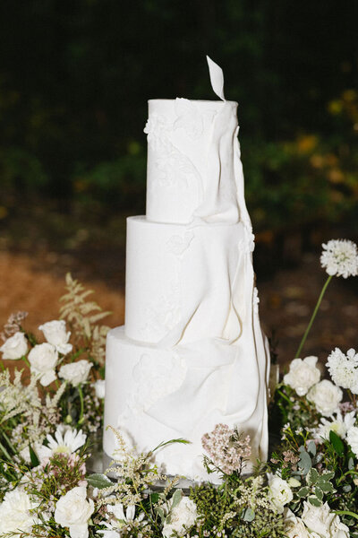 Elegant white wedding cake surrounded by lush white flowers