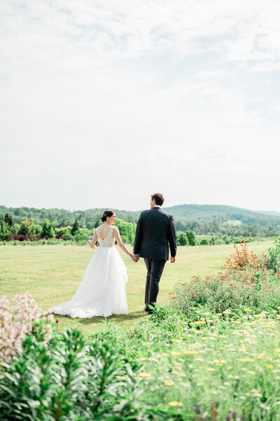 A newlywed couple holding hands and walking in a field