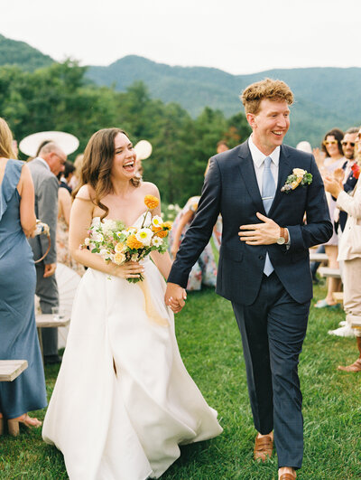 A smiling bride with bouquet and happy groom greet guests after the ceremony by film photographer Megan Lynn of destination photographer My Sun and Stars Co.