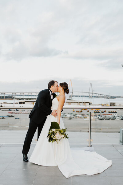 Bride and Groom kissing on the rooftop of the Cedar Room Wedding Venue over looking the Ravenel Bridge captured by Charlotte wedding photographer.