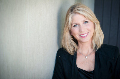 Business headshot of a blonde woman smiling and wearing a black suit.