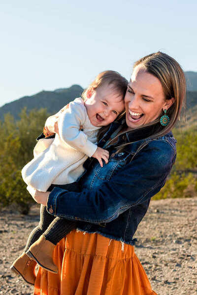 Mom holding infant daughter, laughing together during family portraits in Phoenix, Arizona