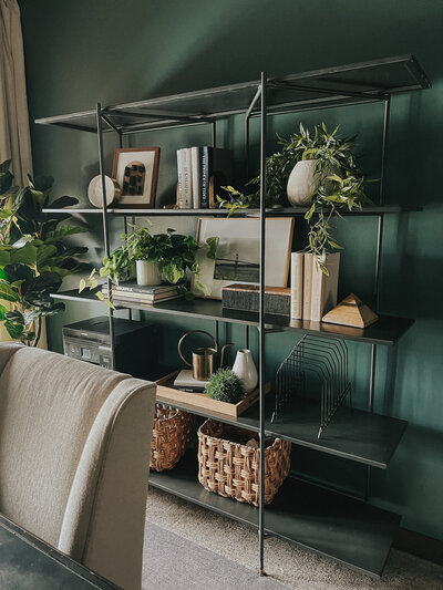 A black metal bookshelf sits behind a grey armchair in an office with green walls