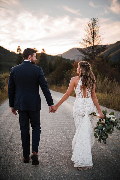 A bride and groom walk hand in hand down a mountain road in western Montana.
