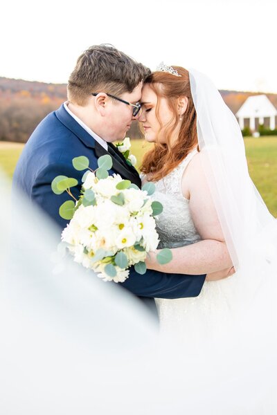 Bride and groom embracing outside as the brides veil sweeps in front of them