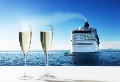 A glass of champagne is in front of a luxury cruise ship sailing on beautiful waters, showcasing elegance and adventure.