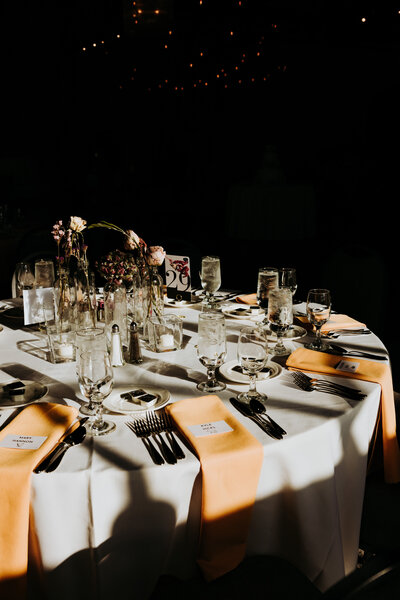 Wedding details of the table set with light orange napkins and the sun glaring onto the table 