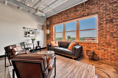 Living room with exposed brick wall and view of downtown in this one-bedroom, one-bathroom luxury condo in the historic Behrens building in Waco, TX.