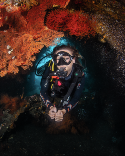 Blonde girl scuba diving and pulling regulator out of mouth towards the camera and smiling