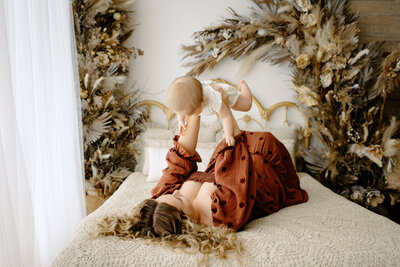 Family photography woman laying in bed on back holding child  with boho background in Tampa Bay, Florida Nadine B Photography