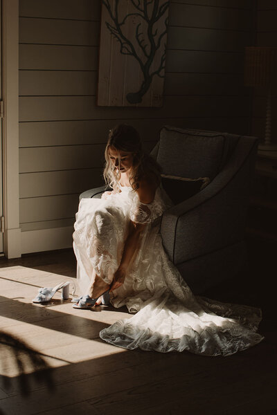 A person in a wedding dress sitting on a chair putting on heels 