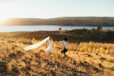 photo of bride and groom walking across open landscape with mountains in the background taken by Wyoming wedding photographer