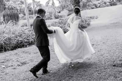 A person holding the train of their partner's wedding dress as they walk 