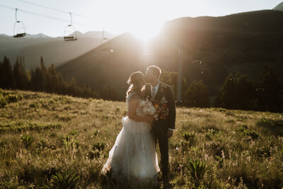 Bride and groom kiss in glowing mountain light beneath ski lifts after their wedding in Breckenridge, Colorado.