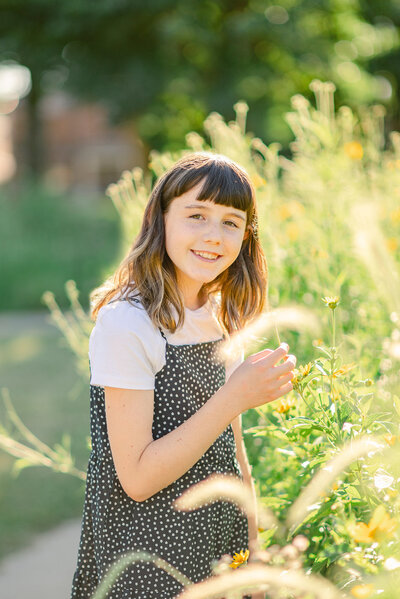 Portrait of a young girl in a black polka dot dress with white t-shirt  standing next to cattails by Chicago family photographer Kristen Hazelton