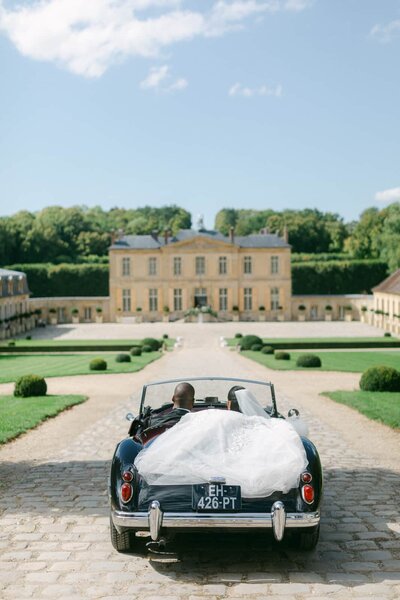 ride and groom driving away from the Chateau de Villette in a vintage convertible under a clear blue sky — Destination Wedding Photographer Portfolio