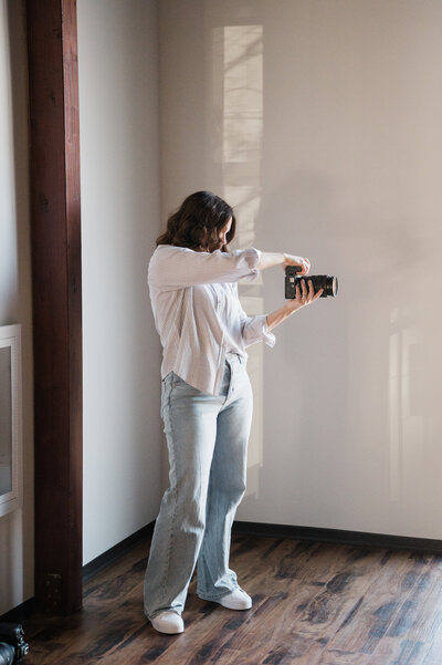 Woman photographing a subject, standing indoors with natural light, as part of a photography mentoring program.