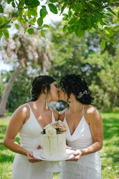 Two-Brides-Kissing-Holding-Wedding-Cake-Miami-Outdoor-Garden-Wedding