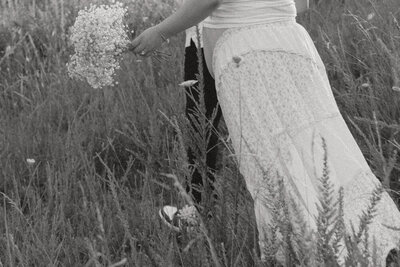 An black and white photo of a couple expecting their first baby walk together in a grassy field at Wing Deer Park in Johnson City, TN. Michaela Crawford Photography, a cinematic maternity photographer located in Northeast, TN. 