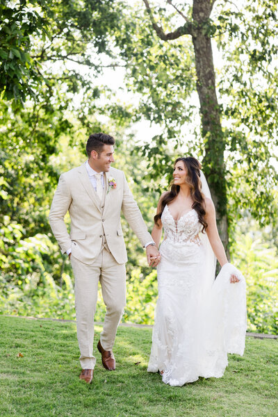 A newlywed couple walk towards the camera as they look at each other adoringly