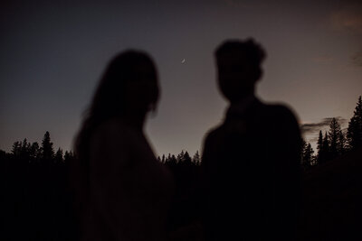 Bride and groom stand with the moon in between their faces