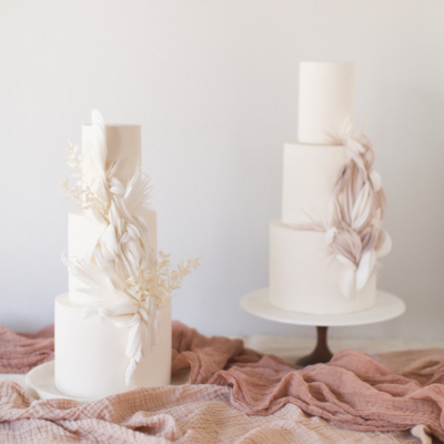 Two neutral three tiered wedding cakes on top of mauve colored gauze