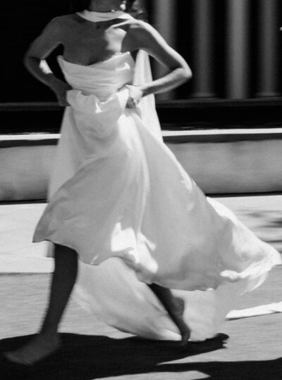 A bride looks over her shoulder while holding up her dress and running barefoot in the street captured by a film wedding photographer