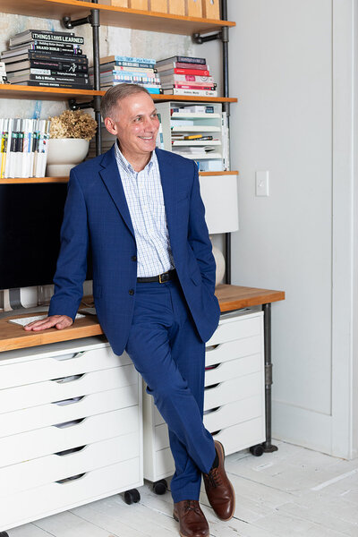 Branding photography man leaning against a desk smiling at someone off camera. 